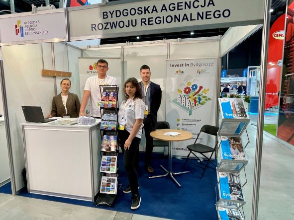 Cztery osoby reprezentujące Bydgoszcz i Bydgoską Agencję Rozwoju Regionalnego na stoisku targowym z materiałami informacyjnymi dla uczestników.