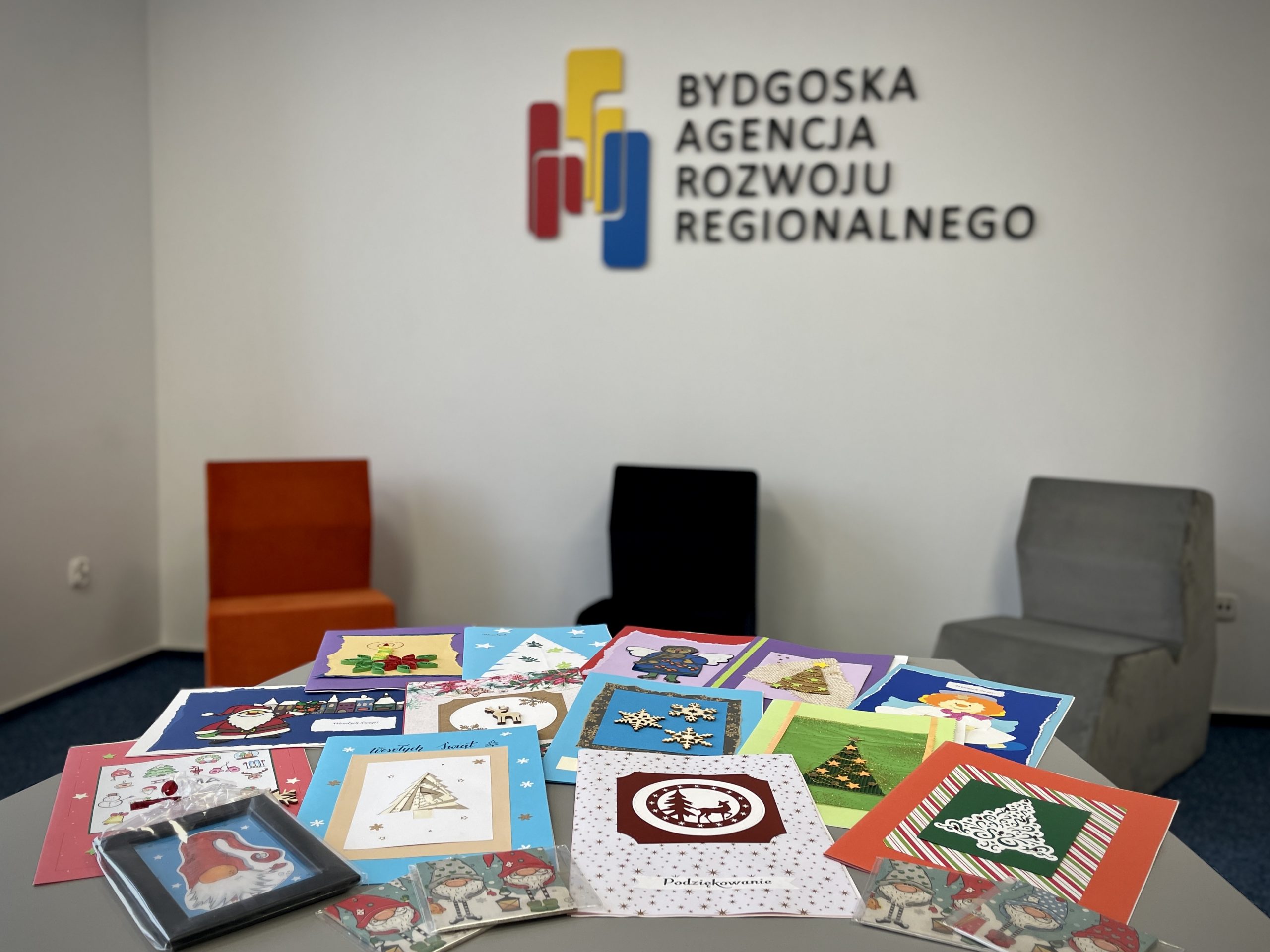 Kolorowe kartki świąteczne wykonane przez dzieci leżą na stole, w tle logo Bydgoskiej Agencji Rozwoju Regionalnego